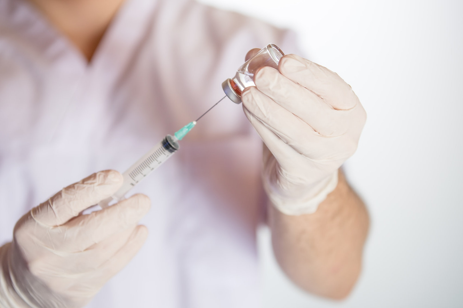 Health worker drawing vaccine in vial into syringe for COVID-19, measles, flu shots