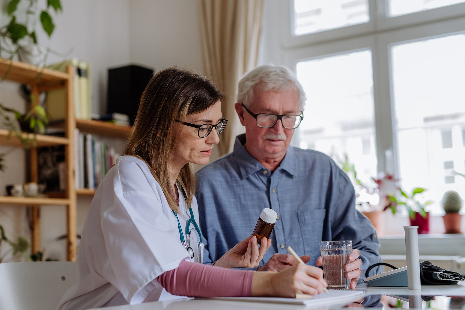 Healthcare worker or caregiver visiting senior man indoors at home, explaining medicine dosage.