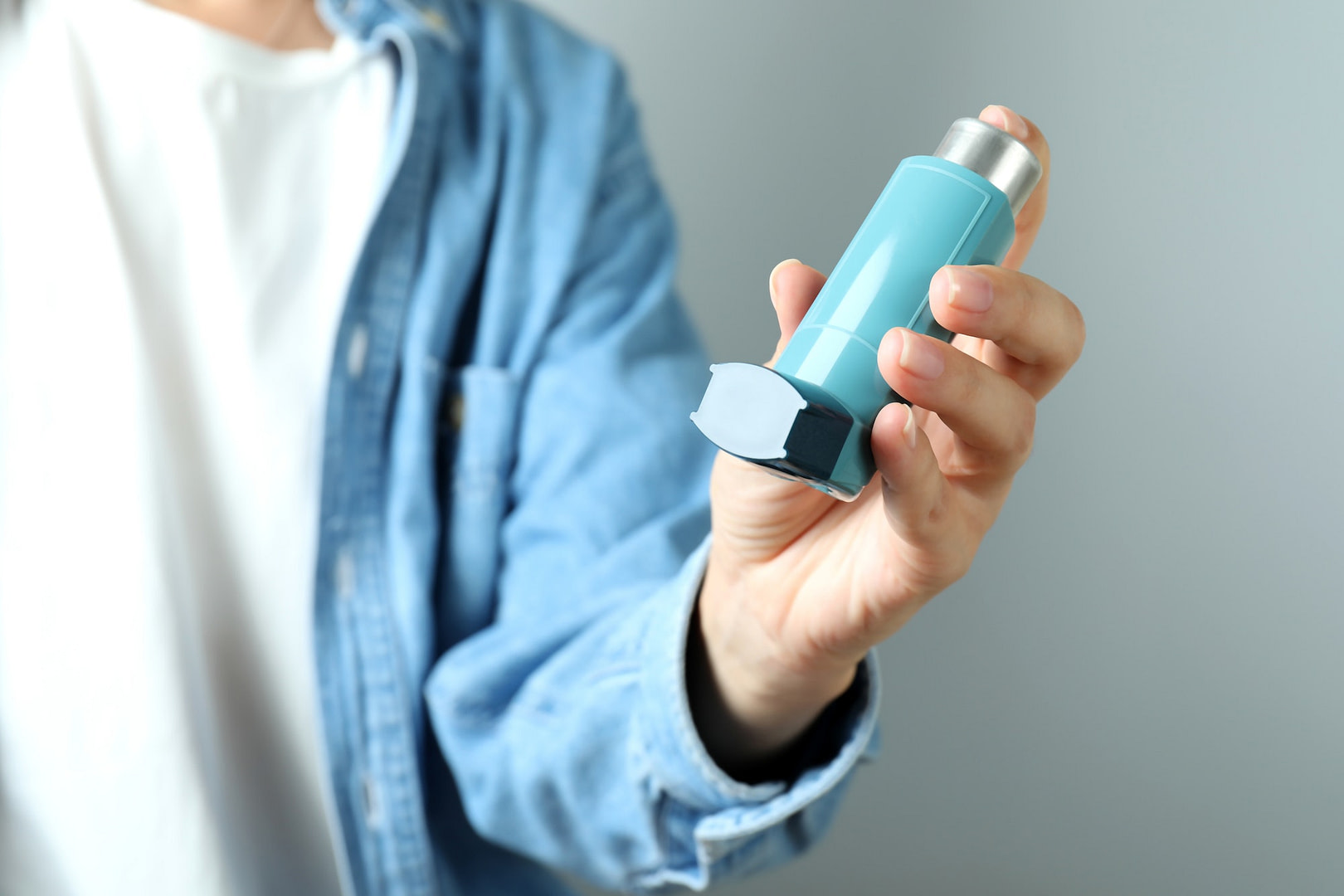 Young woman holds asthma inhaler, close up