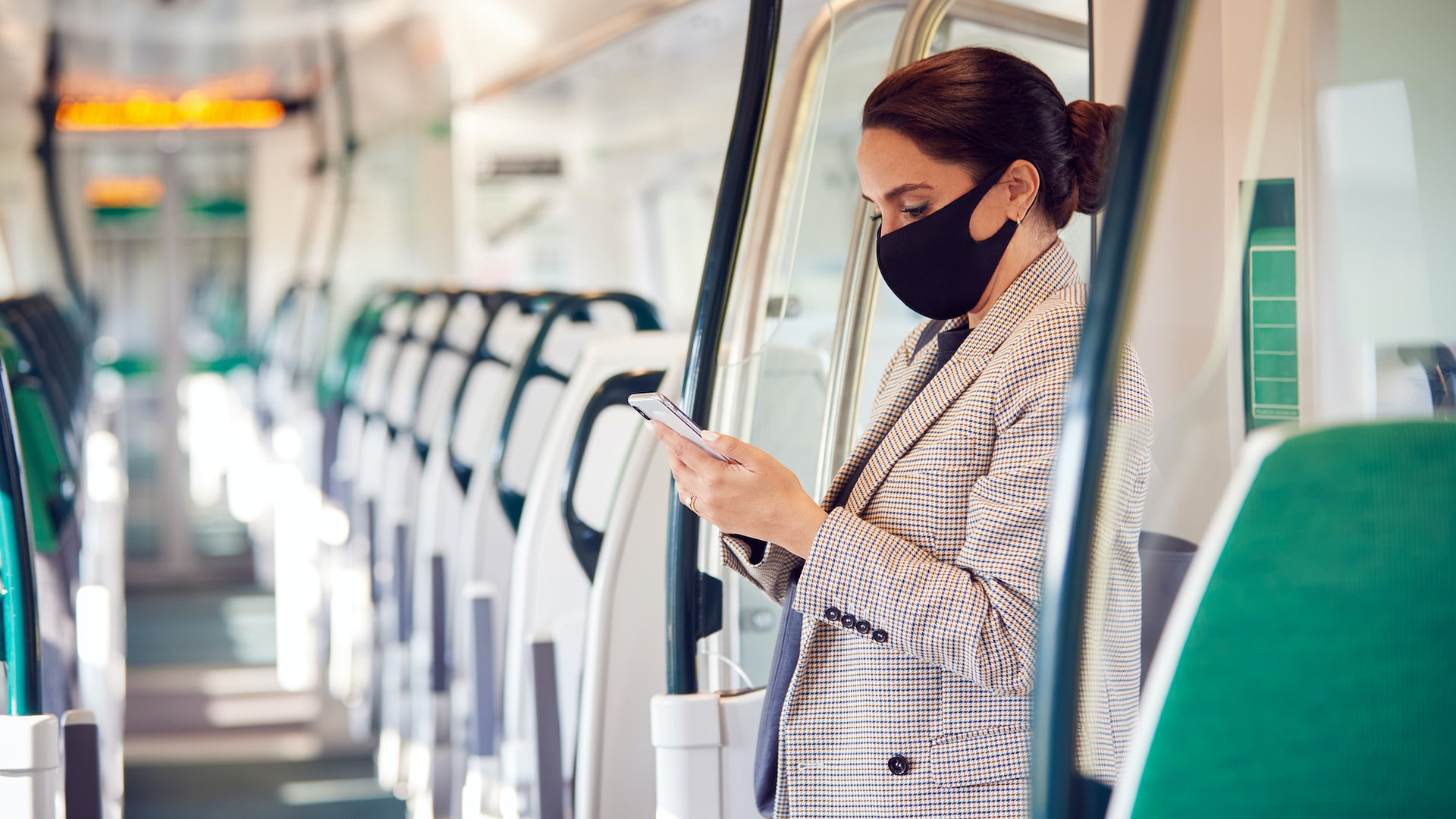 Businesswoman Stands In Train Carriage Using Mobile Phone Wearing PPE Face Masks During Pandemic