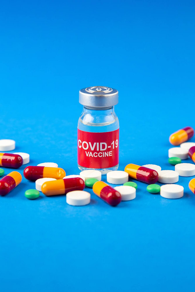 Vertical view of COVID- vaccine in medical ampoule pills capsules on dark and soft blue background