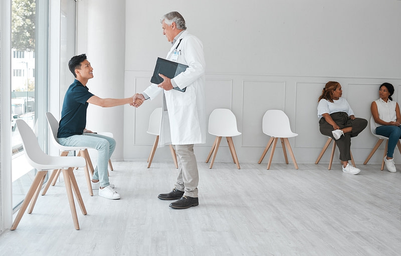 Shot of a mature doctor shaking hands with a young man in the waiting room of a clinic